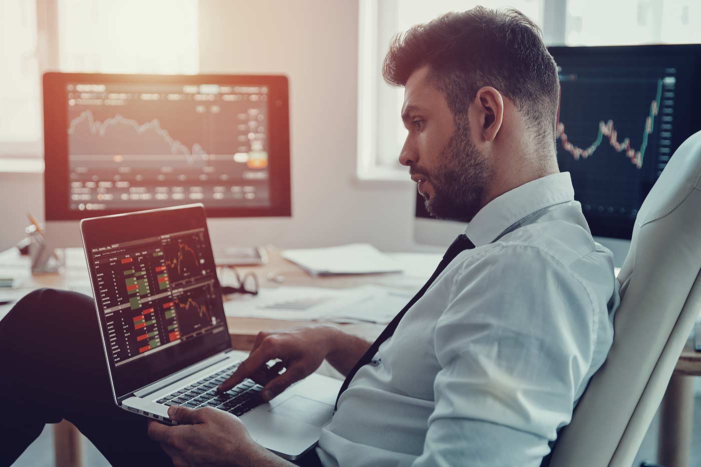 Thoughtful but relaxed day trader making money earning living by studying stocks on laptop perched on his lap