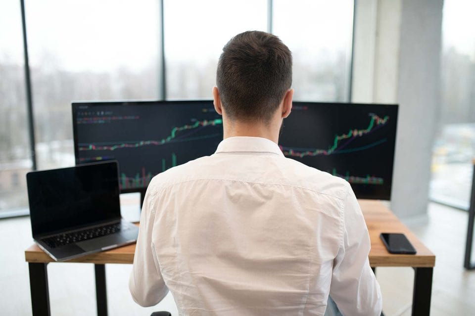 Close up of day trader working at desk with chart patterns for financial markets on screens