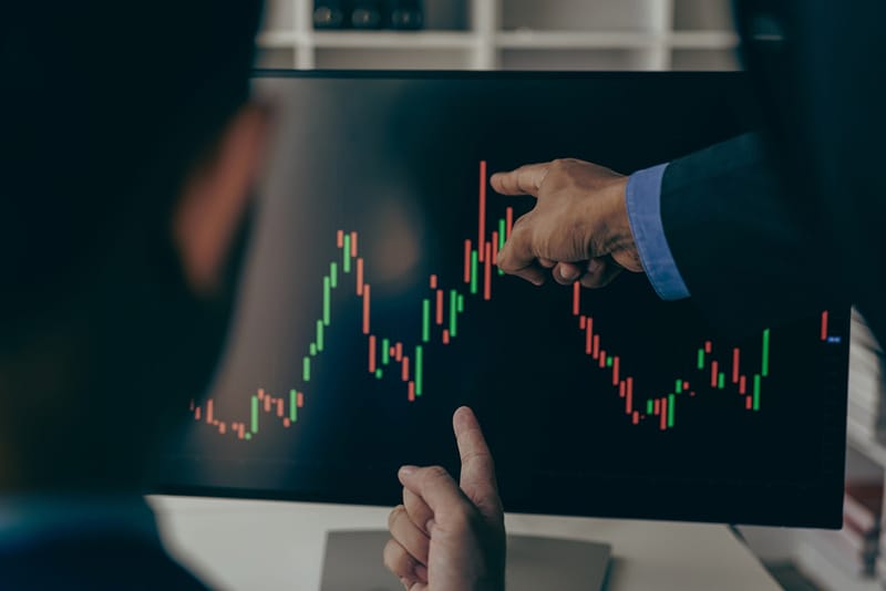 Two day traders in suits inspecting candlestick chart on computer screen  