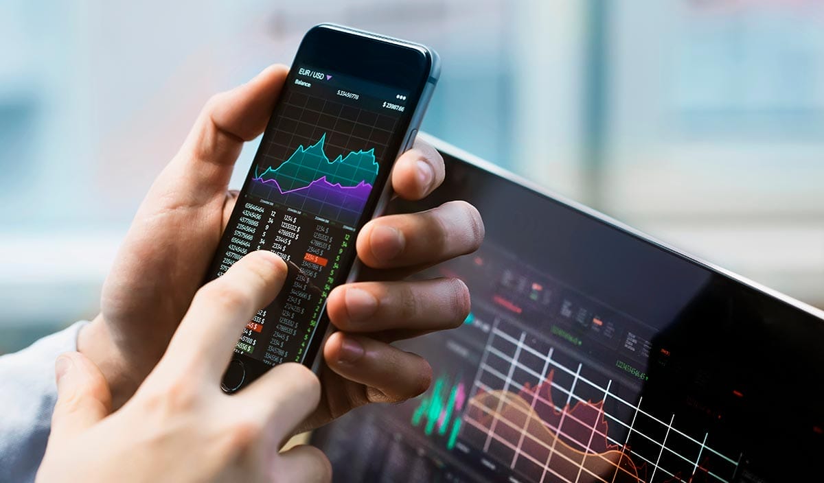 Day trader holding phone and looking at Forex trading chart patterns